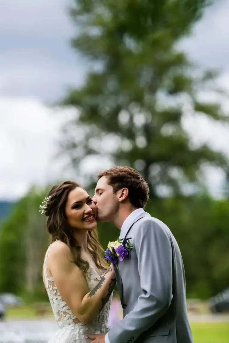 Newlywed kissing their smiling partner’s cheek outdoors