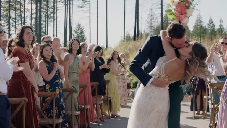 Newlyweds kissing in the aisle as wedding guests applaud