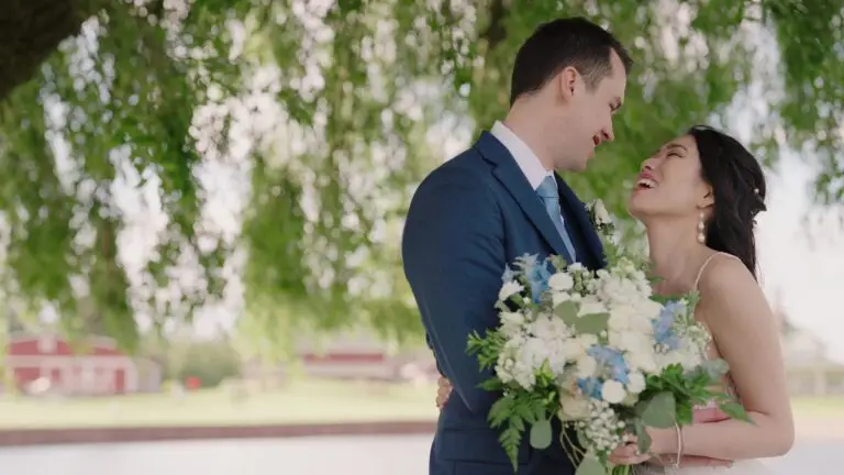Newlyweds laughing beneath willow branches with a bouquet